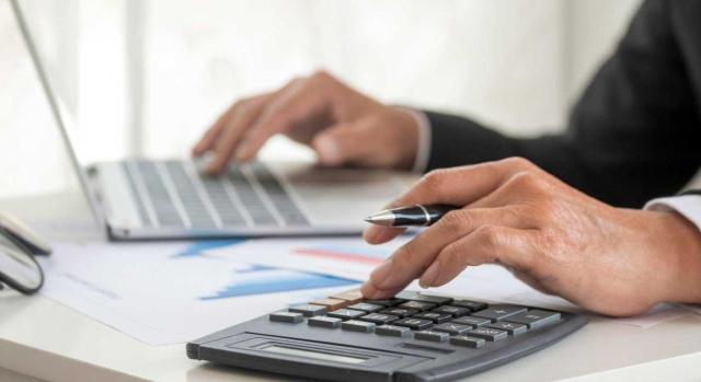 Actualización NIA-ES 2026: Cambios en el Informe de Auditoría Nuevos cambios en el Informe de Auditoría: El ICAC actualiza las NIA-ES. Imagen de un hombre trabajando con su portátil y calculadora