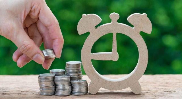 Inversión Inversión. Reloj despertador de madera y una mano haciendo una pila de monedas al lado
